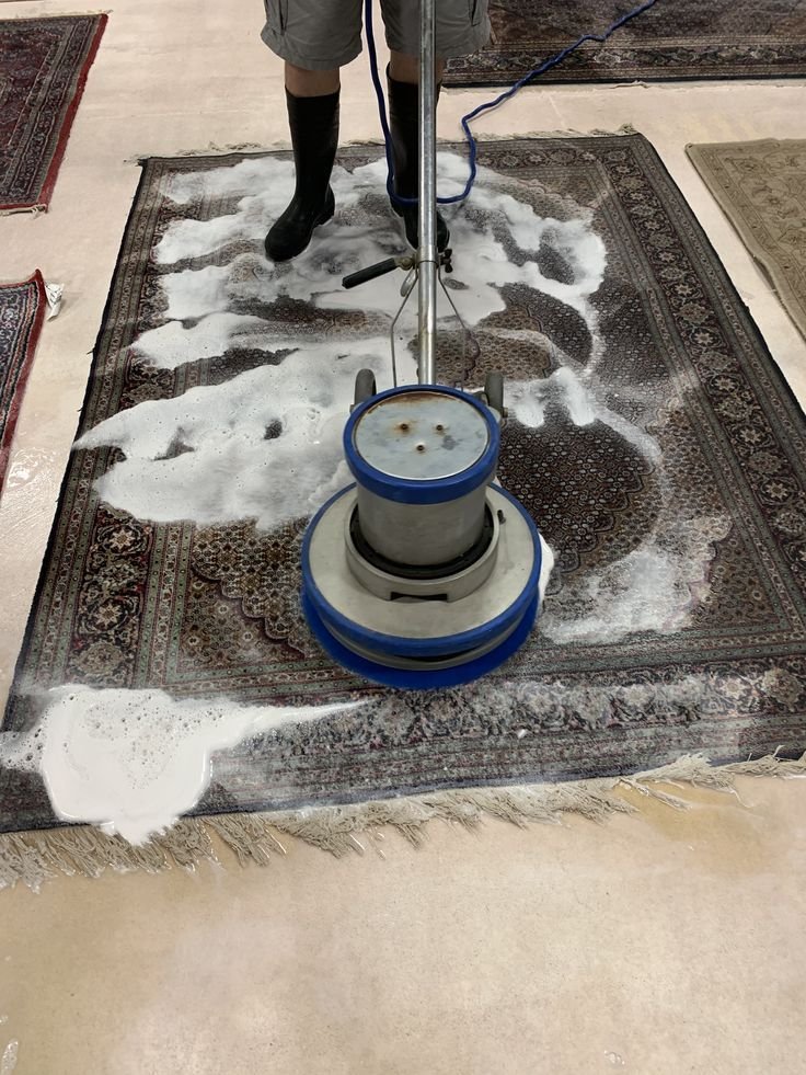 Professional technician cleaning a carpet using a rotary carpet cleaning machine with foam treatment