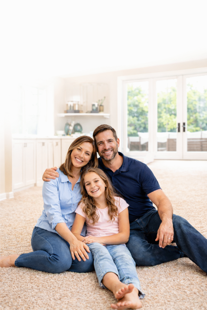 Happy family sitting on freshly cleaned carpet in living room showing satisfaction with professional carpet cleaning service.