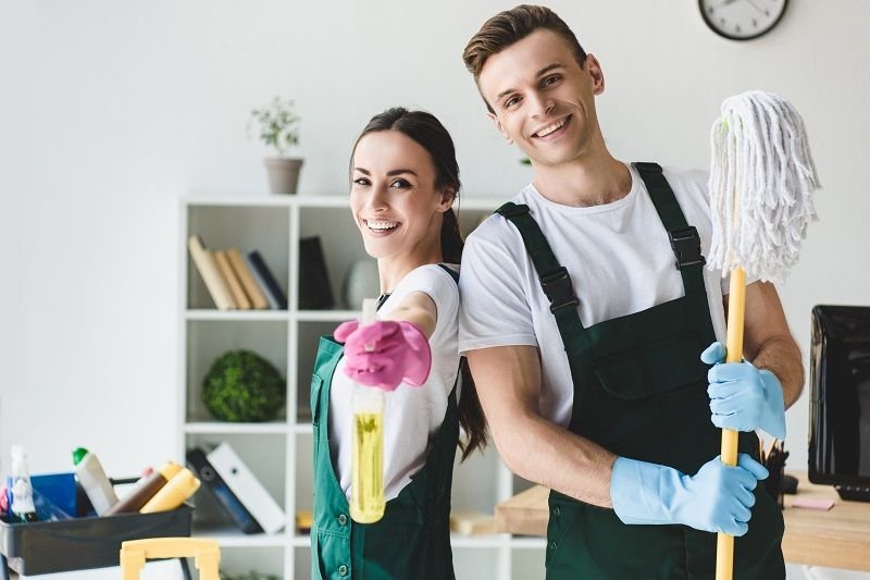 Professional cleaning team holding cleaning tools and supplies in a modern home