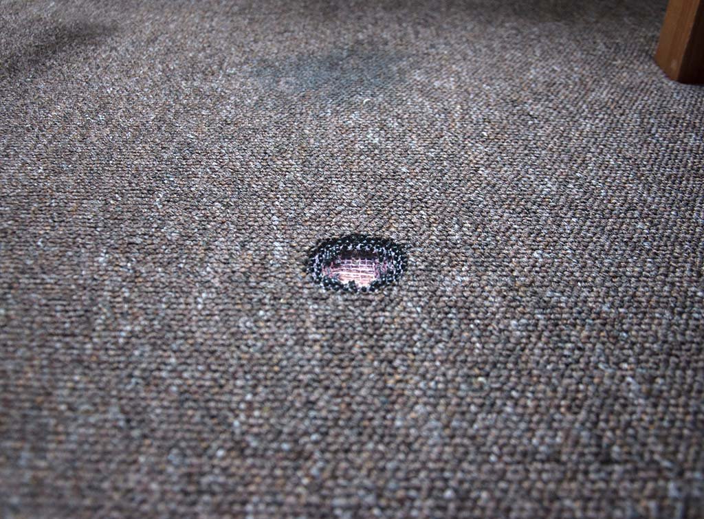 Burn hole damage on carpet requiring repair or patching service