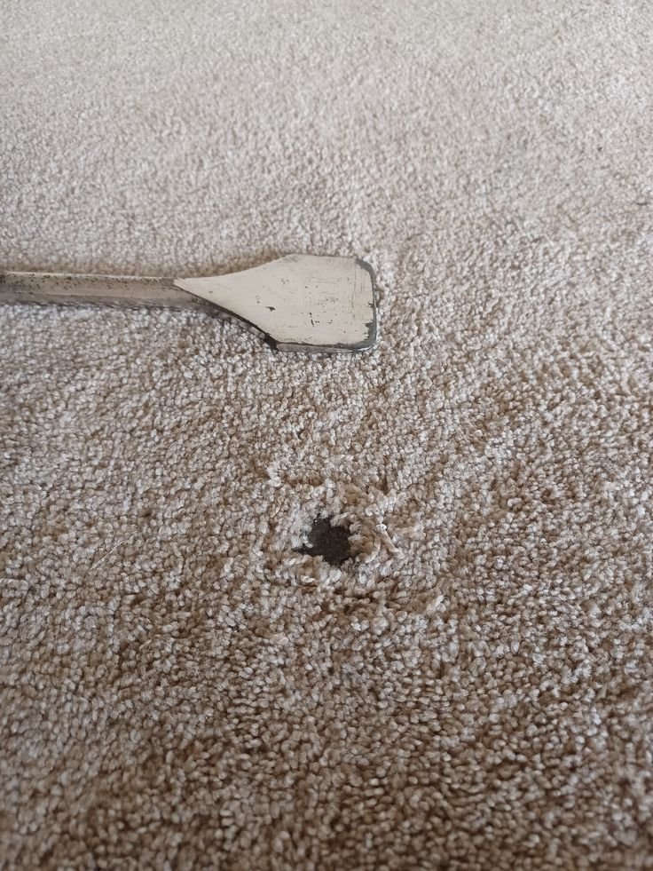 Close-up of a damaged carpet with a small hole before professional carpet repair in a Melbourne home, showing frayed carpet fibres ready for seamless patch restoration.