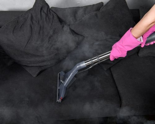 cropped shot of person in rubber gloves cleaning sofa with vacuum cleaner and hot steam